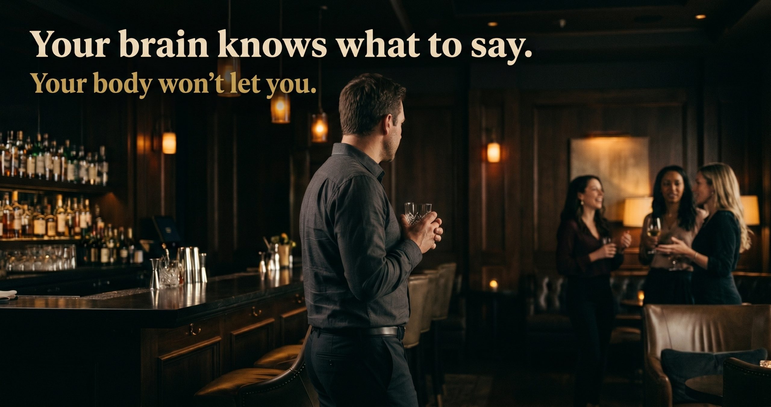 Man standing alone at a bar holding his drink while women talk across the room illustrating approach anxiety