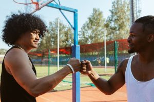 How to be more confident: be a team player. Two men fist-bump on a basketball court.